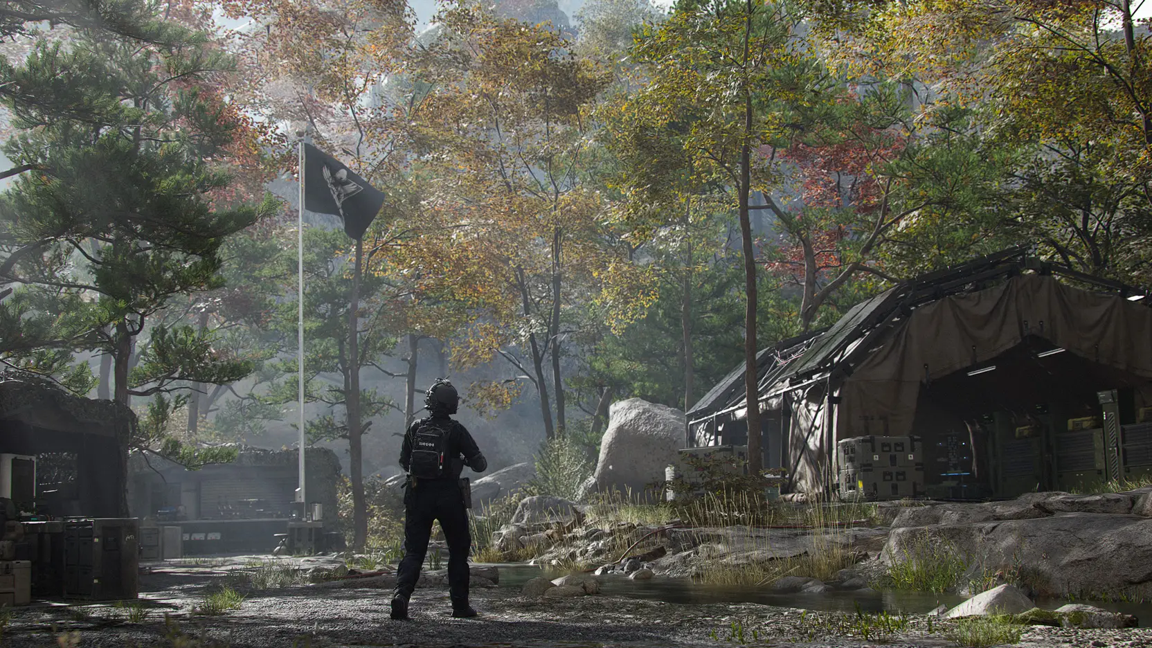 An armed operator stands on a gravel path in a wooded camp, facing a flagpole and a large military tent.